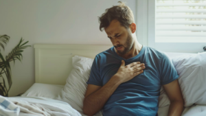 Homem sentado na cama, sofrendo dores no peito